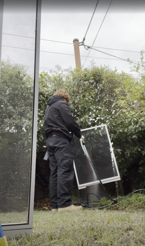 Justin cleaning a fly screen with a pressure hose in a Melbourne backyard